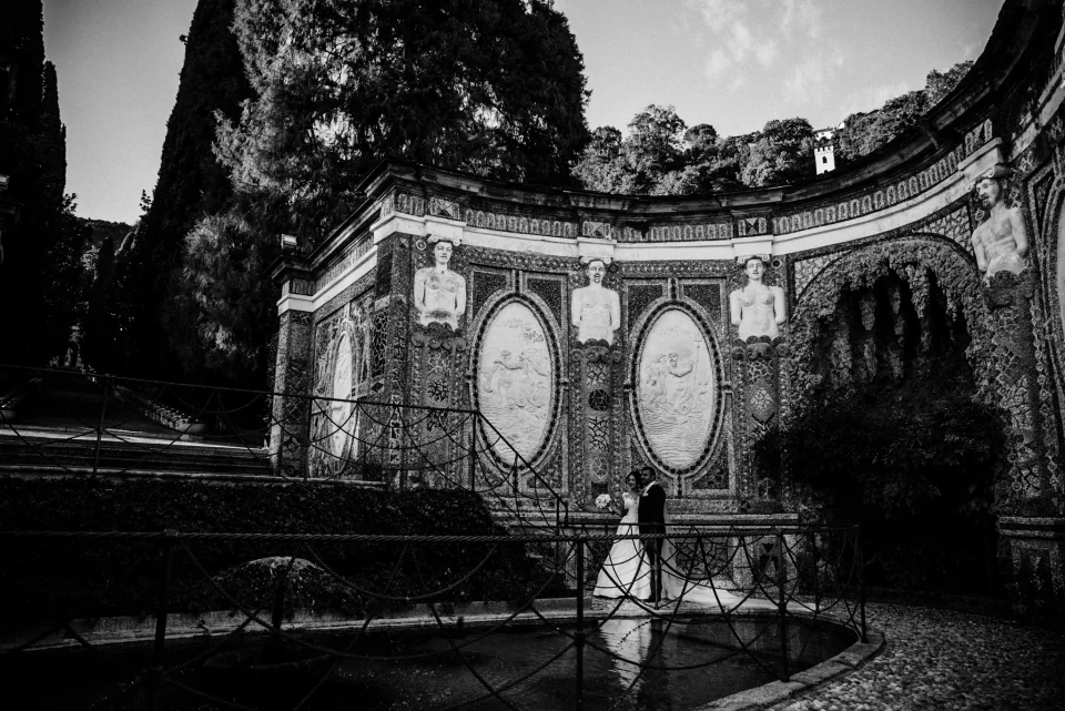 Newlyweds together on a curved garden bridge beneath decorative statues.
