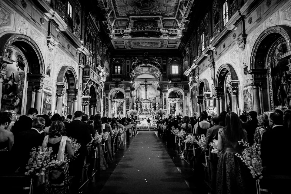 A wedding ceremony with guests seated in an ornate church, in black and white.