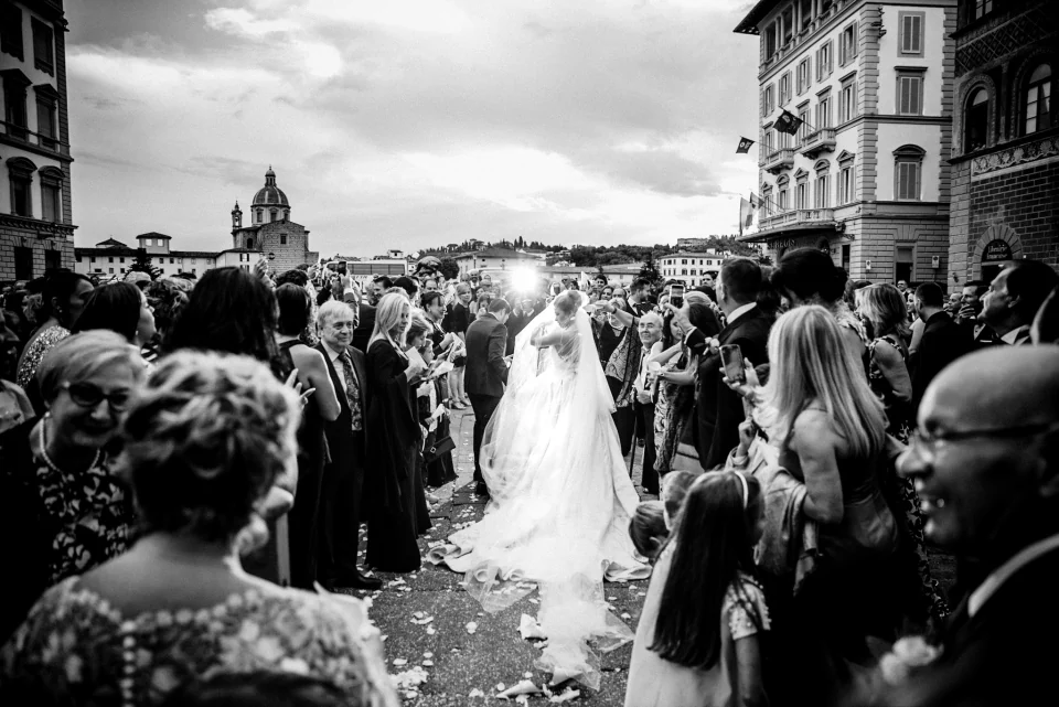 Newlyweds emerging into a crowd of wedding guests, in black and white.