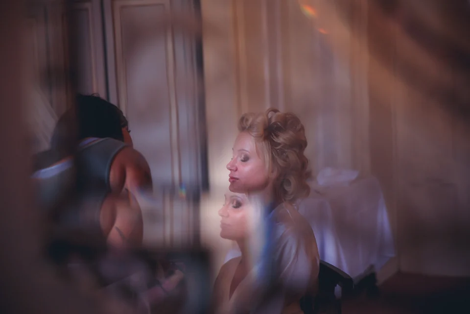 A bride during makeup preparations, seen through soft colored reflections.